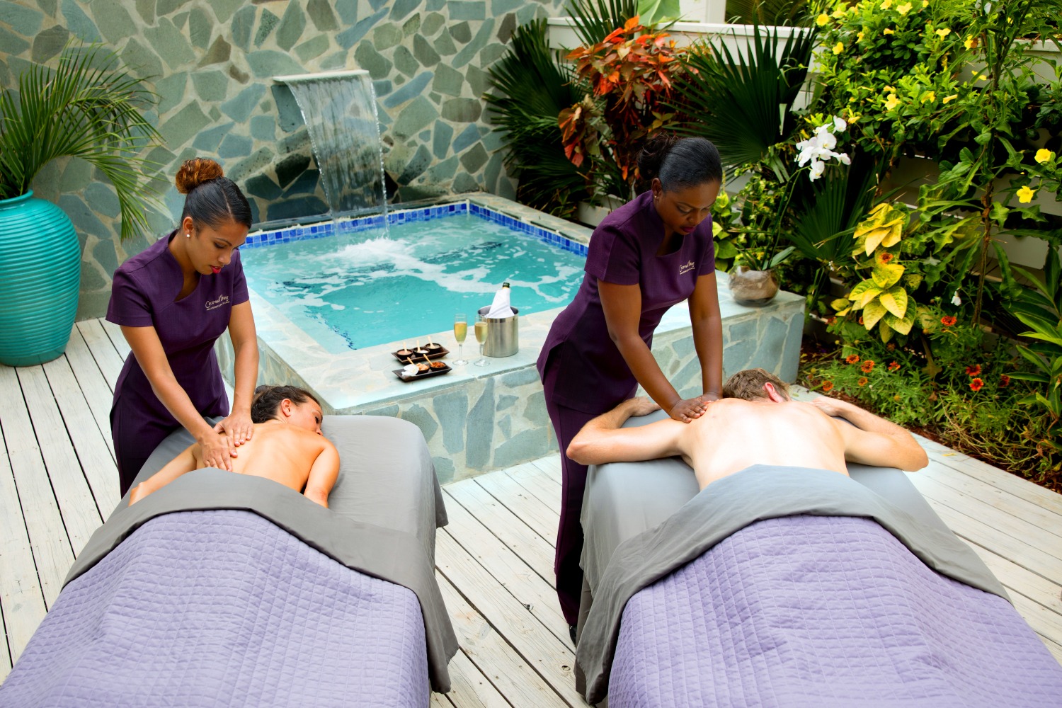Couples enjoy relaxing massages by a tranquil poolside, surrounded by greenery and a water feature.