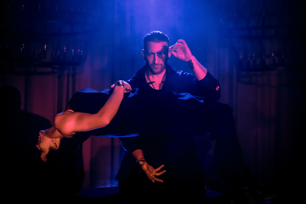 A magician performs an illusion with a woman levitating on a stage under dramatic blue lighting at Salvage City Supper Club.