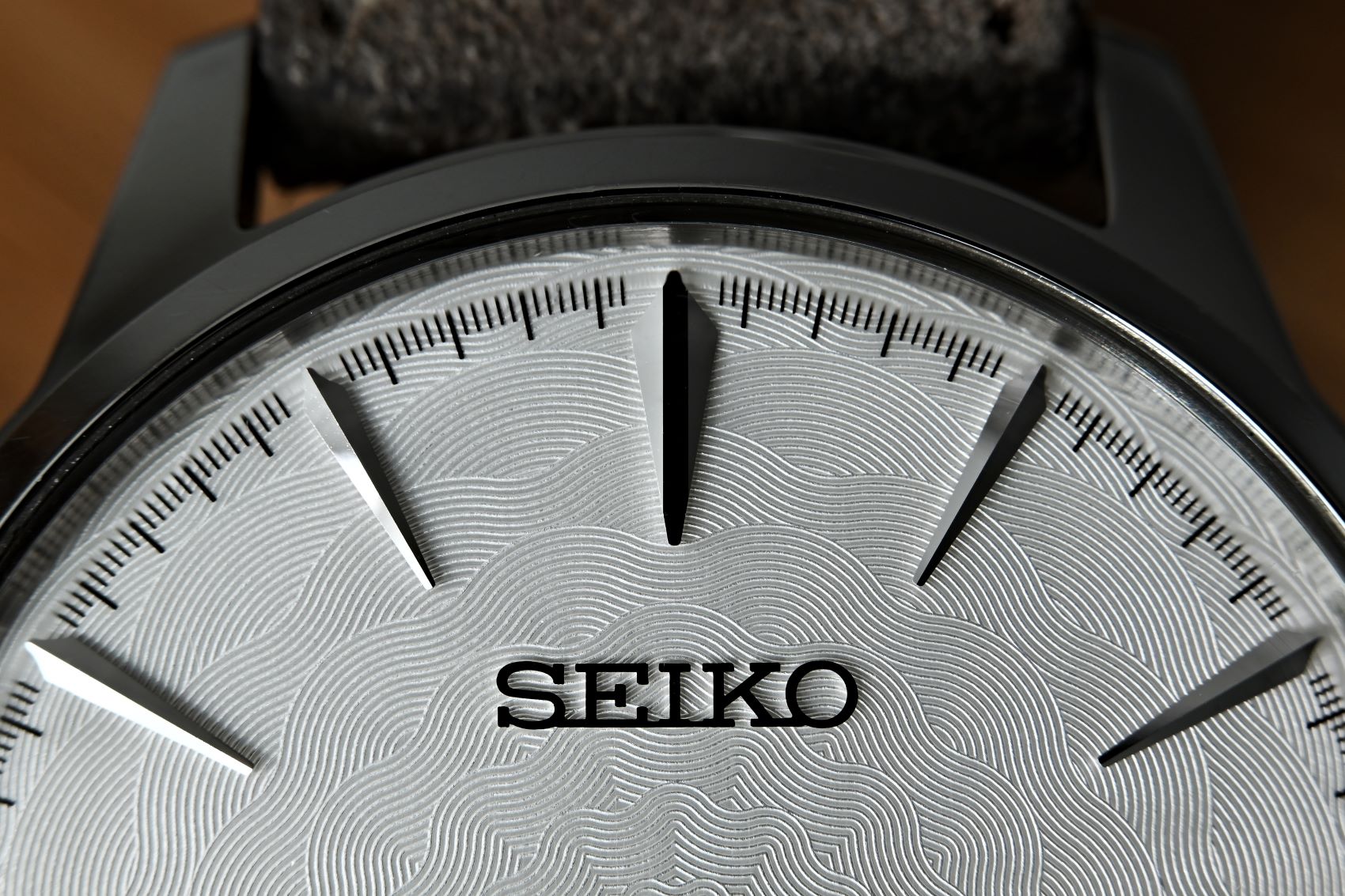 Seiko watch dial featuring wave-pattern texture and sharp silver hour markers against a silver background.