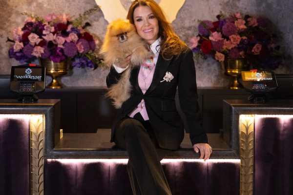 Lisa Vanderpump poses elegantly at The Vanderpump Hotel, holding a small dog against a backdrop of flowers and sophisticated decor.