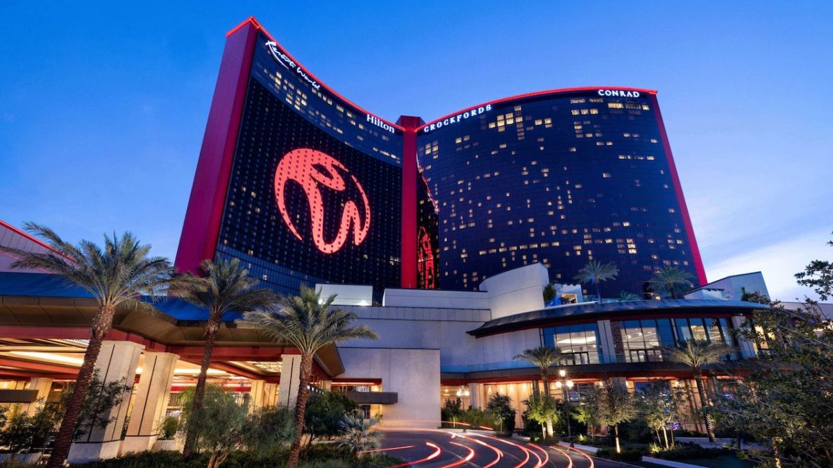 Luxury Conrad hotel entrance at Resorts World Las Vegas under evening sky with illuminated signage and palm trees.