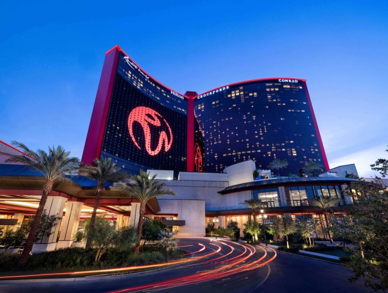 Luxury Conrad hotel entrance at Resorts World Las Vegas under evening sky with illuminated signage and palm trees.