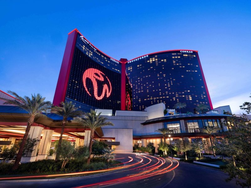 Luxury Conrad hotel entrance at Resorts World Las Vegas under evening sky with illuminated signage and palm trees.