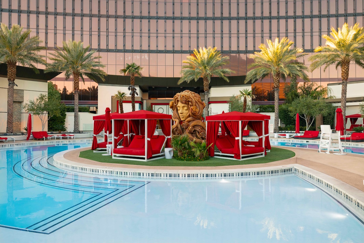 Luxurious pool area at Conrad Resort World Las Vegas featuring red cabanas, palm trees, and elegant landscaping.