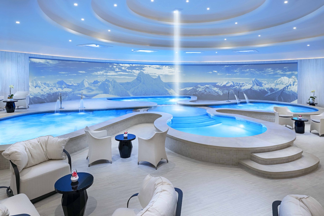 Spa area featuring multiple pools, contemporary seating, and a mountain backdrop, designed for relaxation and luxury indulgence.
