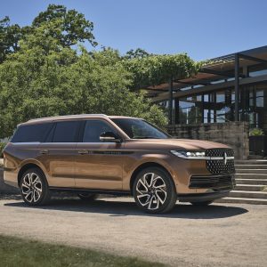 2026 Lincoln Navigator in Sunrise Copper parked in front of a modern building, surrounded by greenery and clear blue skies.