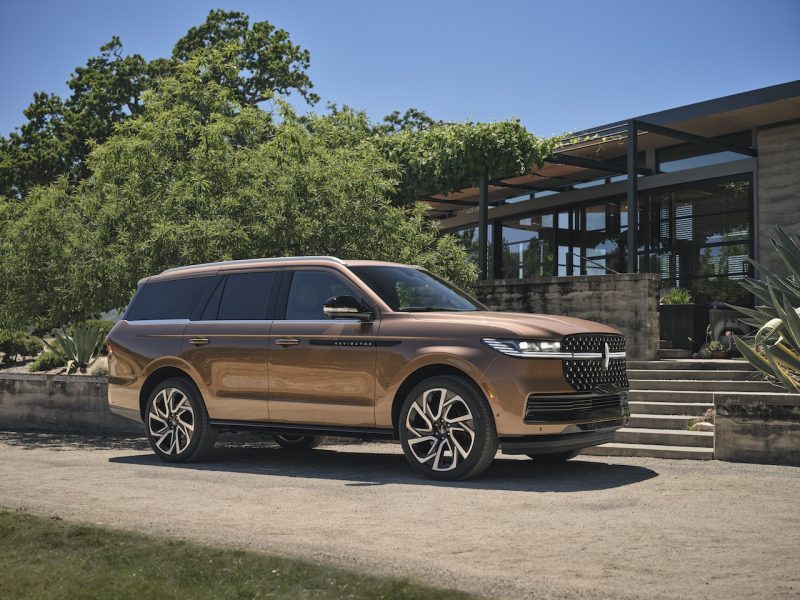 2026 Lincoln Navigator in Sunrise Copper parked in front of a modern building, surrounded by greenery and clear blue skies.