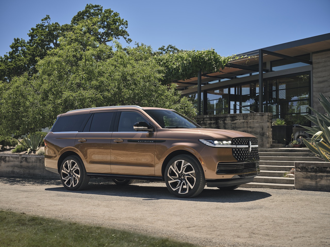 2026 Lincoln Navigator in Sunrise Copper parked in front of a modern building, surrounded by greenery and clear blue skies.