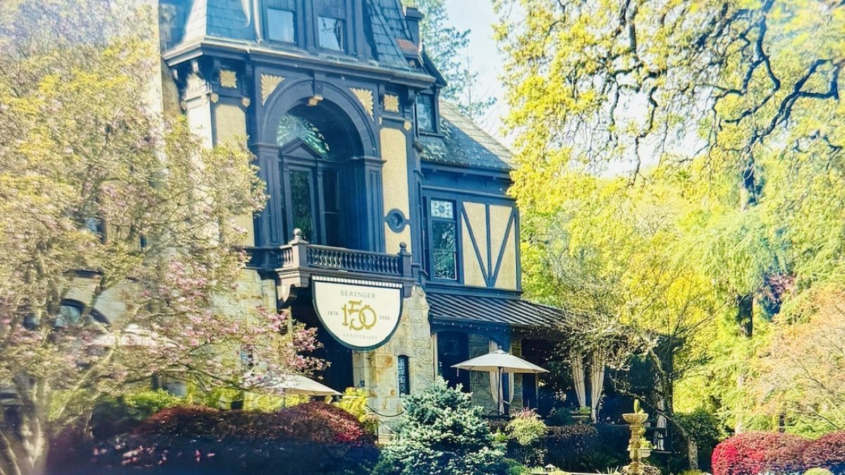 Beringer Winery's historic building adorned with a 150th anniversary sign, surrounded by lush greenery and colorful landscaping.