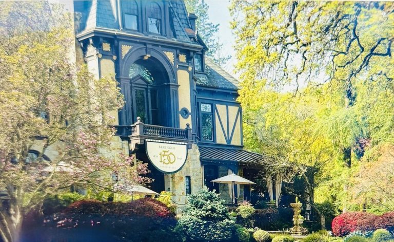 Beringer Winery's historic building adorned with a 150th anniversary sign, surrounded by lush greenery and colorful landscaping.