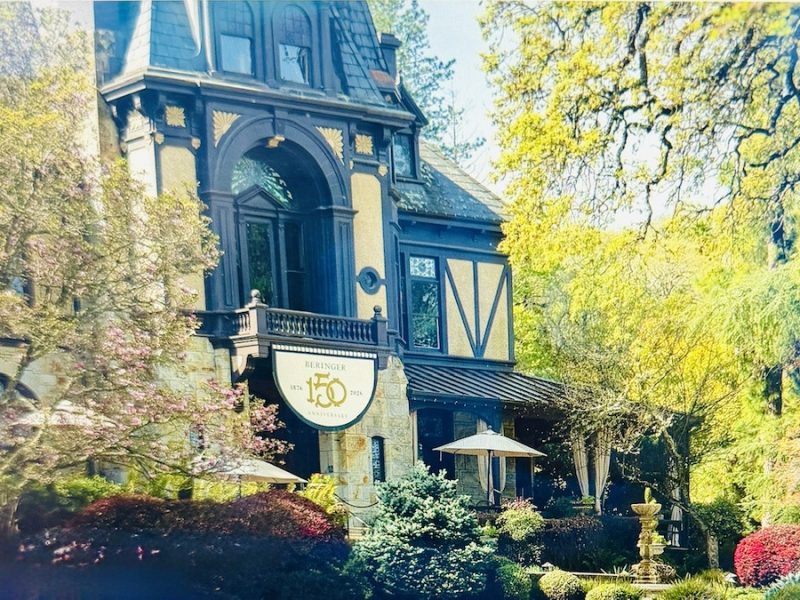 Beringer Winery's historic building adorned with a 150th anniversary sign, surrounded by lush greenery and colorful landscaping.