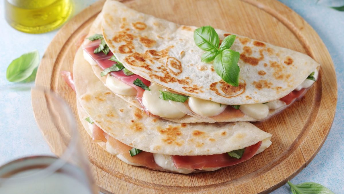 Protein wraps filled with ham, cheese, and basil on a wooden serving board, highlighting a nutritious meal option.