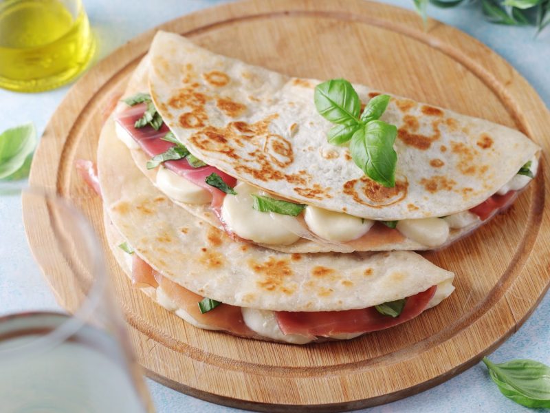 Protein wraps filled with ham, cheese, and basil on a wooden serving board, highlighting a nutritious meal option.
