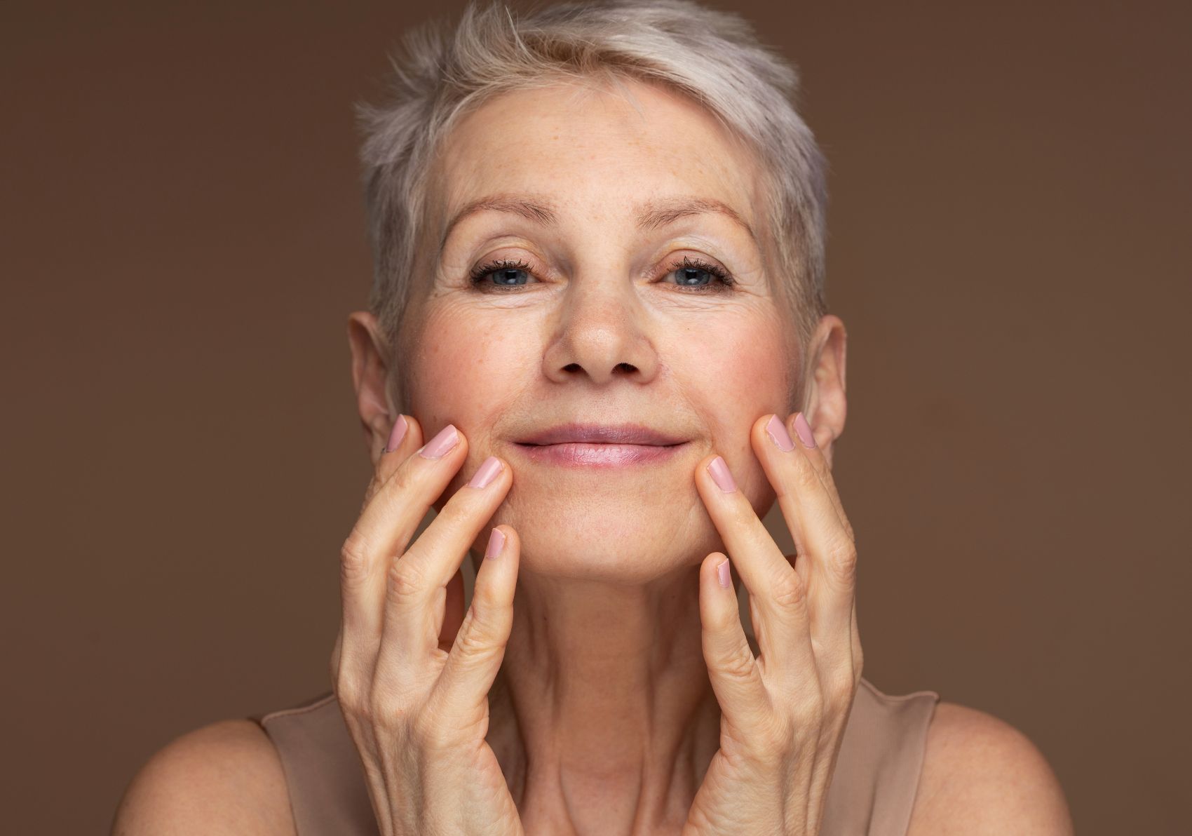 Mature woman applying illuminating primer makeup with a gentle smile and a soft touch to her face.