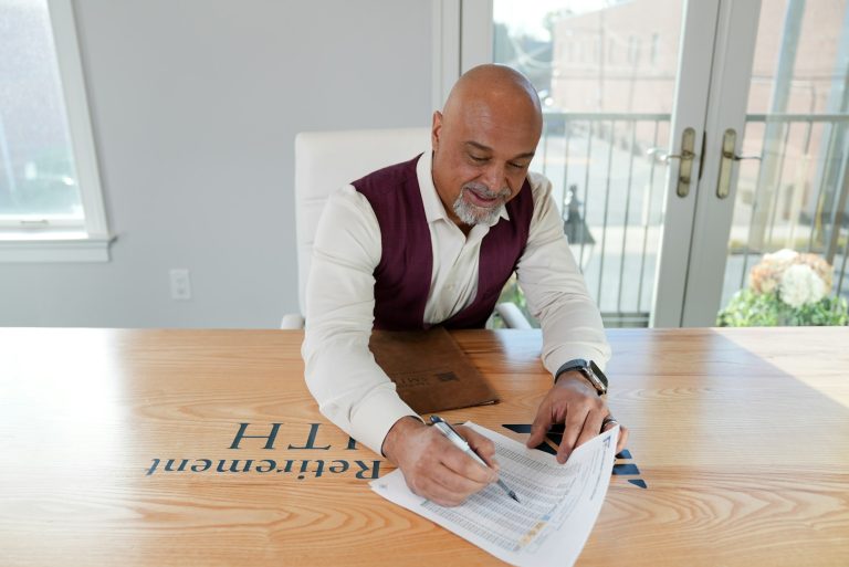 Man signing documents at a wooden table with a retirement plan logo, focusing on financial details and planning.