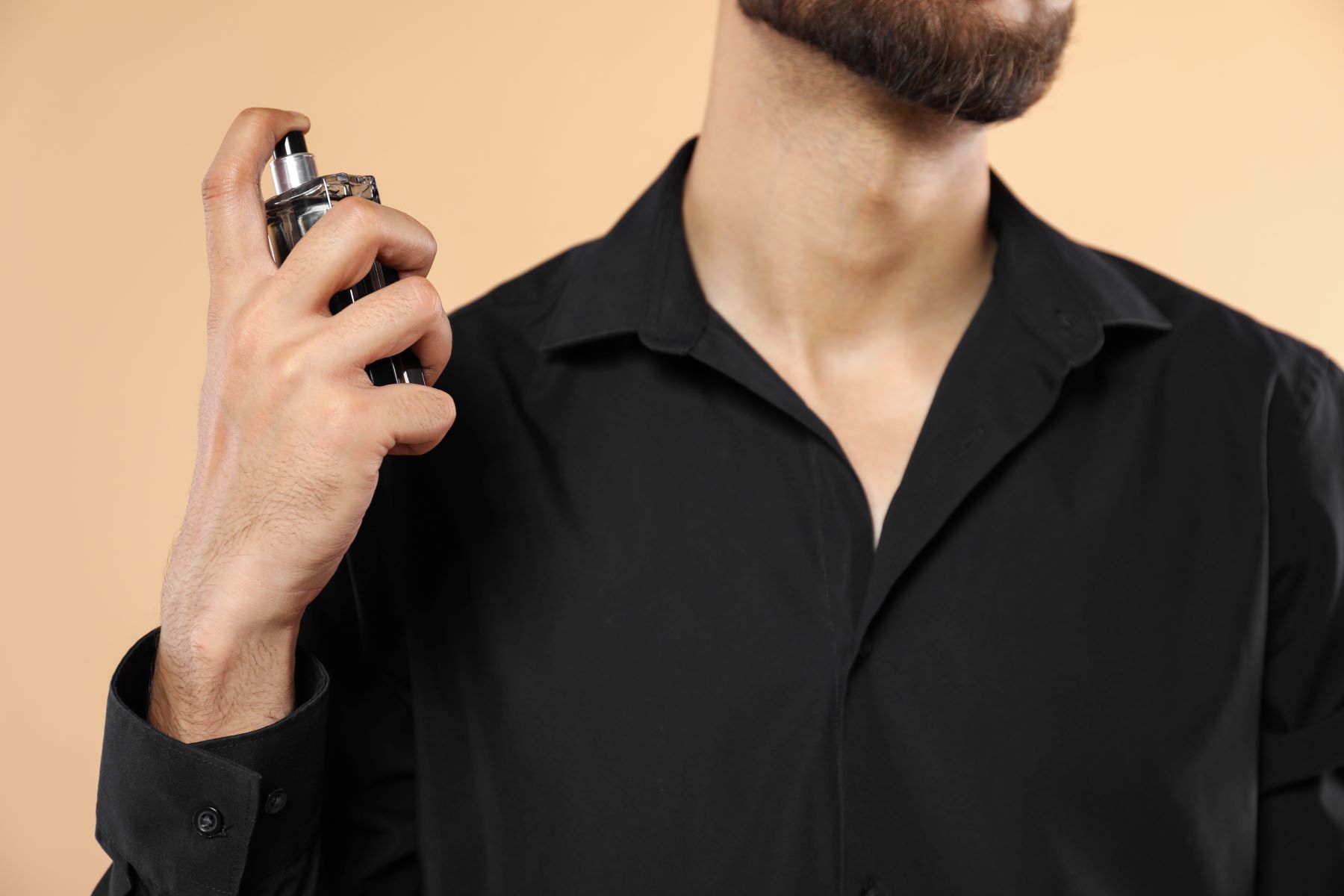 Man in a black shirt spraying perfume, highlighting the allure of long-lasting fragrances for men in 2026.