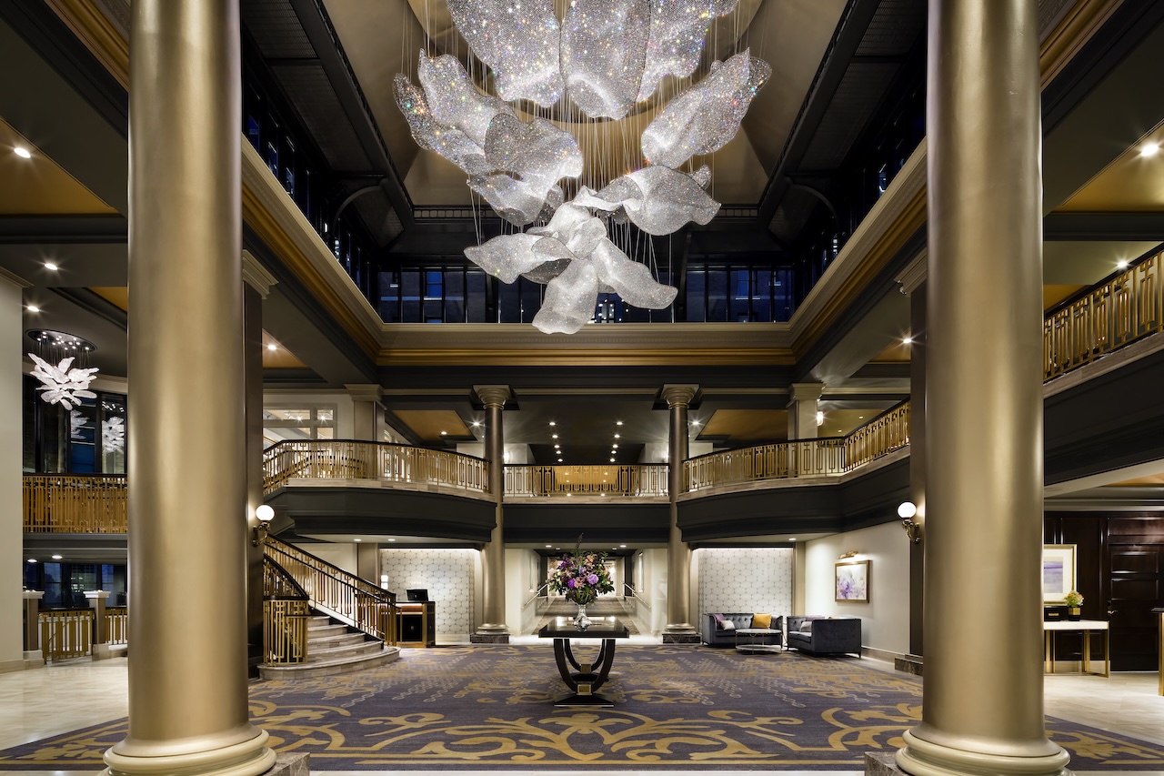 Elegant hotel lobby featuring a striking chandelier, polished columns, and refined seating areas, showcasing luxury and sophistication.