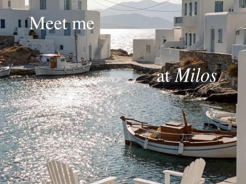 Chairs by a serene waterfront in Milos, with boats and white buildings reflecting a summer vibe.