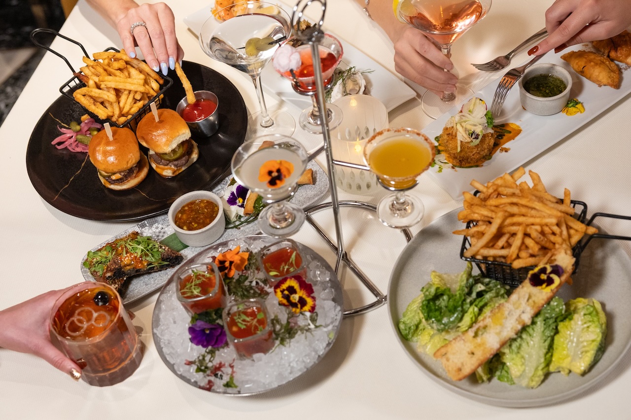 A variety of gourmet dishes including sliders, fries, cocktails, and salads, beautifully presented on a dining table.