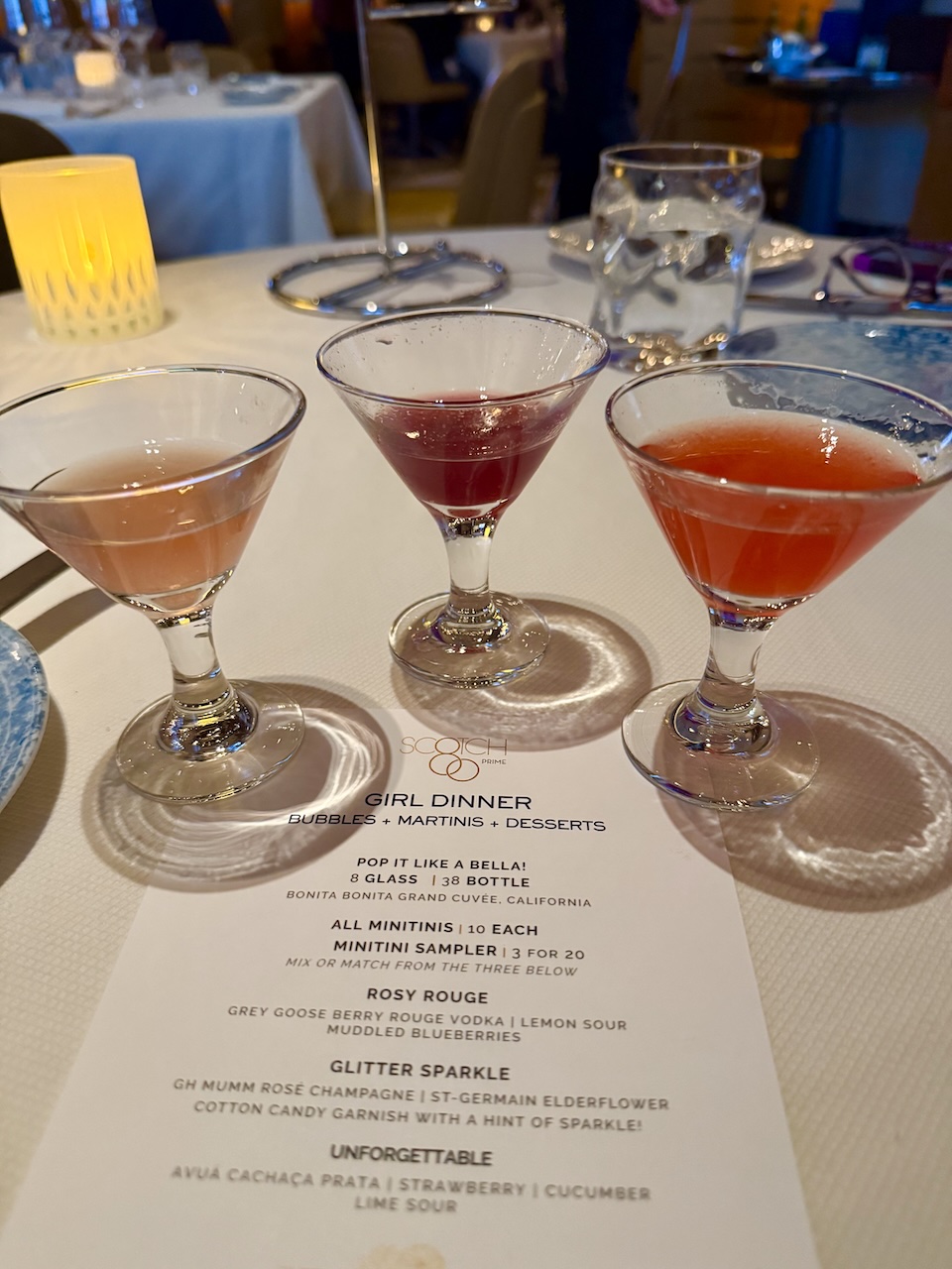 Three colorful cocktails in martini glasses on a dining table, accompanied by a dinner menu from Scotch 80 Prime at Palms Las Vegas.