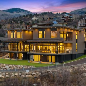 Modern mountain home at Steamboat's base, featuring large windows and a stylish exterior illuminated at dusk.