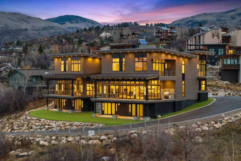 Modern mountain home at Steamboat's base, featuring large windows and a stylish exterior illuminated at dusk.