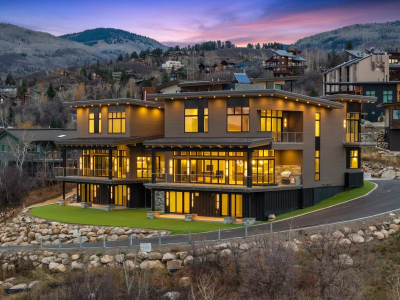 Modern mountain home at Steamboat's base, featuring large windows and a stylish exterior illuminated at dusk.