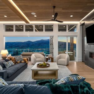 Modern living room featuring a stylish sofa, cozy chairs, and expansive windows showcasing mountain views at sunset.