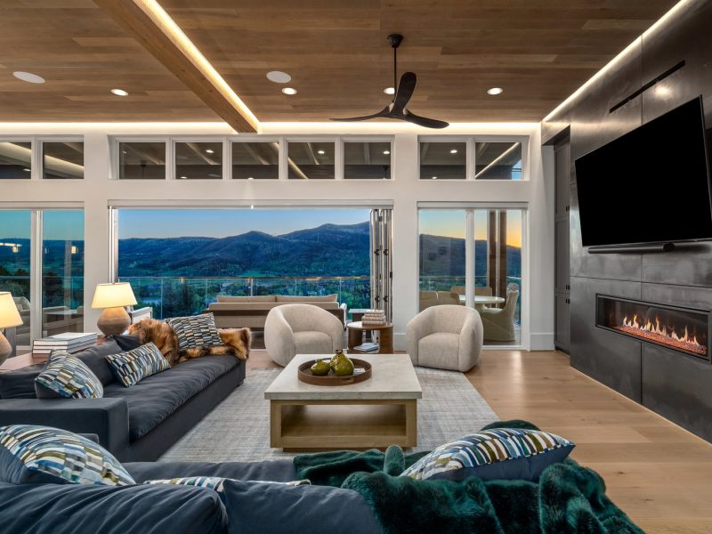 Modern living room featuring a stylish sofa, cozy chairs, and expansive windows showcasing mountain views at sunset.