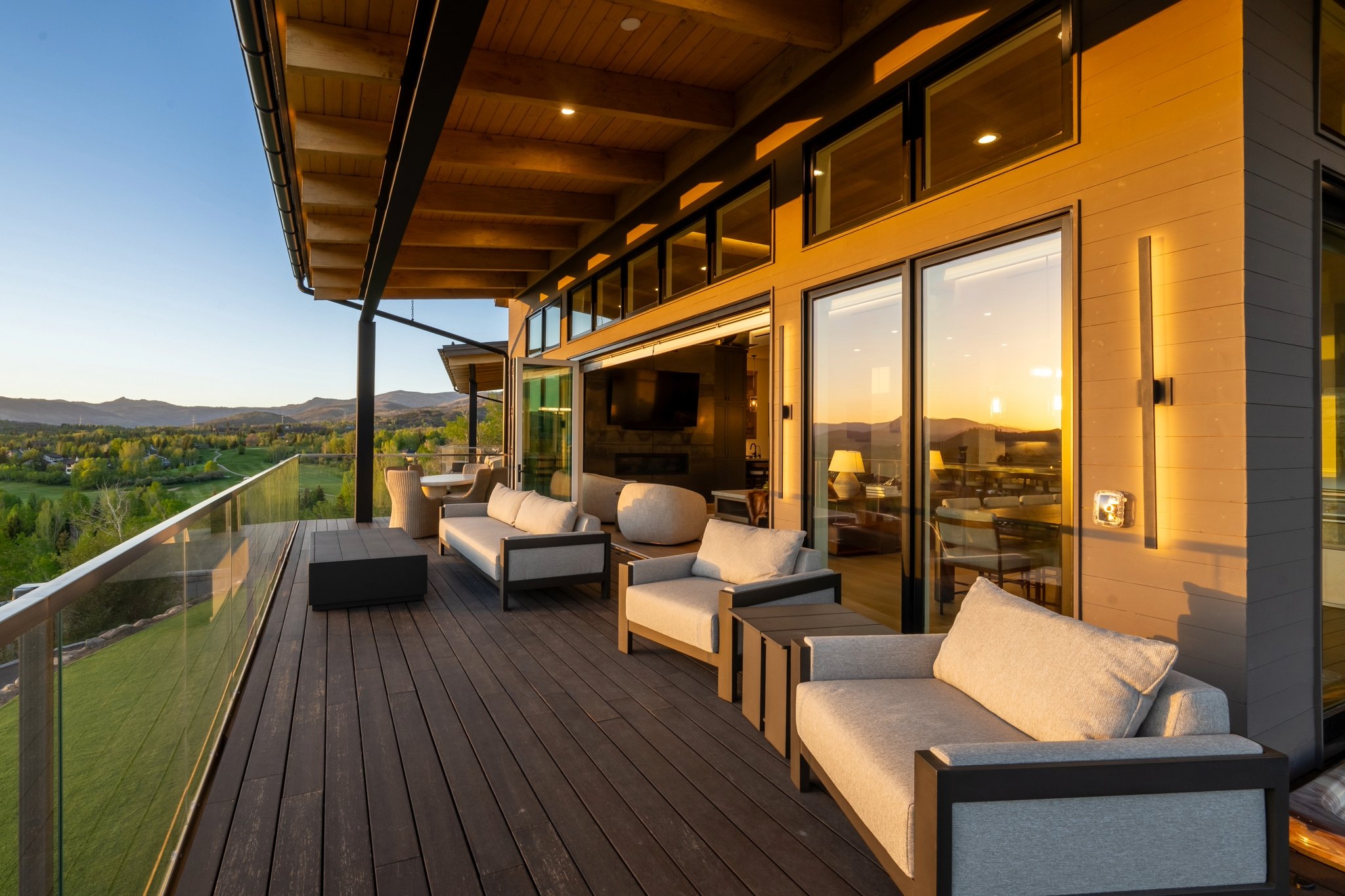 Modern seating area on a deck overlooks lush landscape and mountains at sunset, showcasing new architectural design.