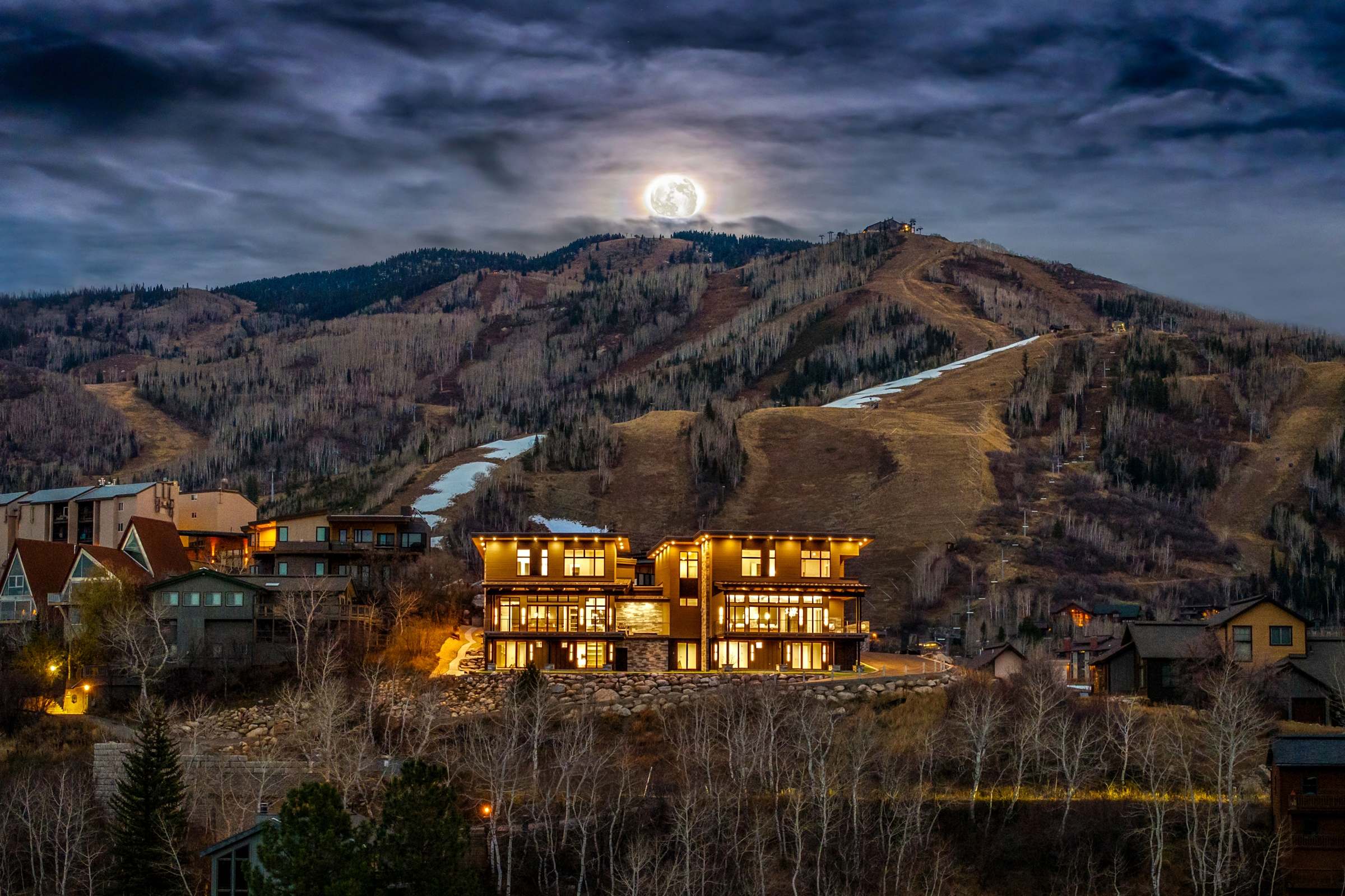 New architectural home illuminated at Steamboat's mountain base under a full moon, showcasing the surrounding landscape.
