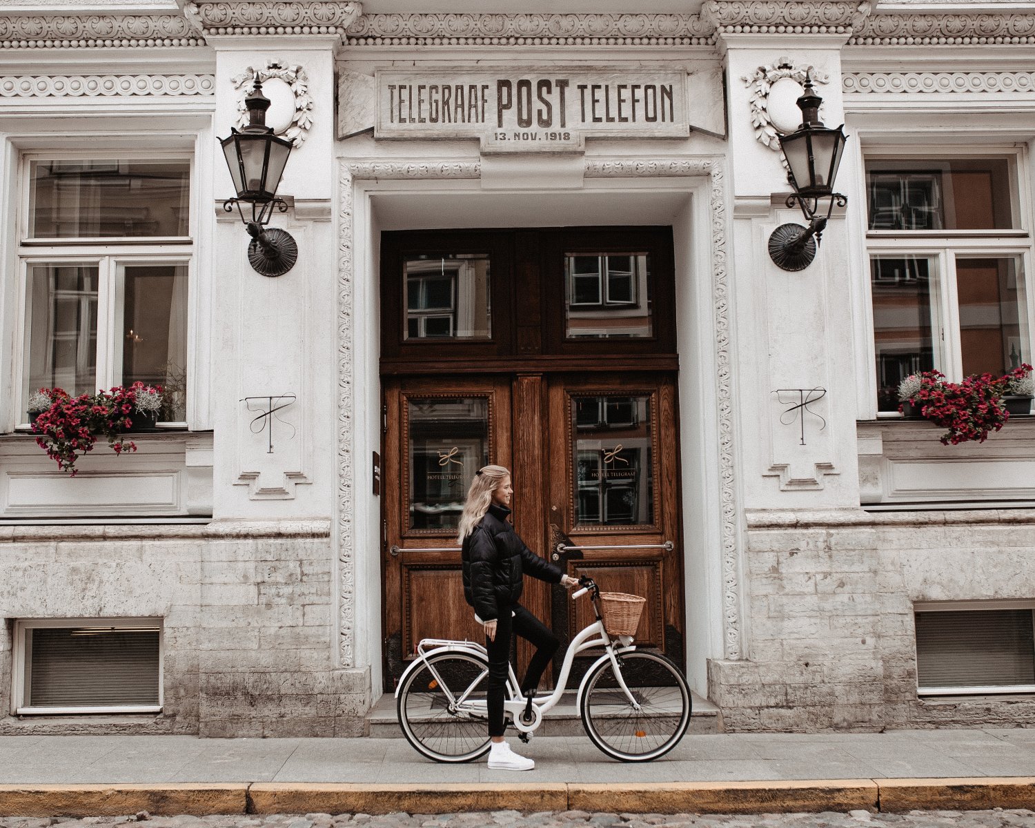 A cyclist stands beside a white bicycle in front of the historic Hotel Telegraaf, adorned with flowers and lanterns.