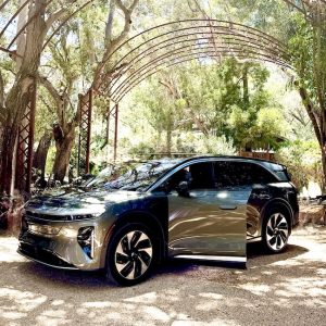 Lucid Gravity SUV parked under a decorative archway surrounded by trees, highlighting its sleek design and open door.