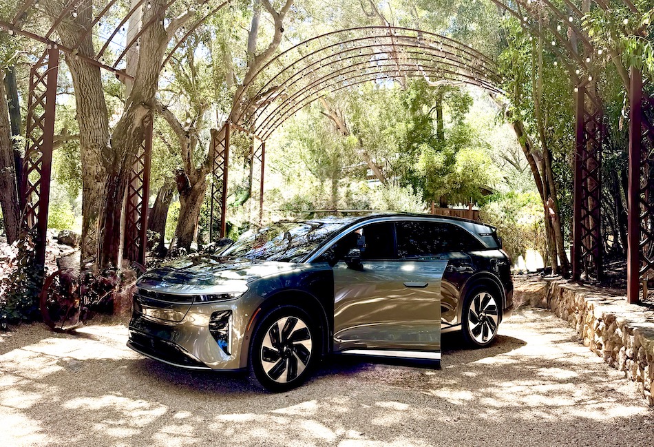 Lucid Gravity SUV parked under a decorative archway surrounded by trees, highlighting its sleek design and open door.