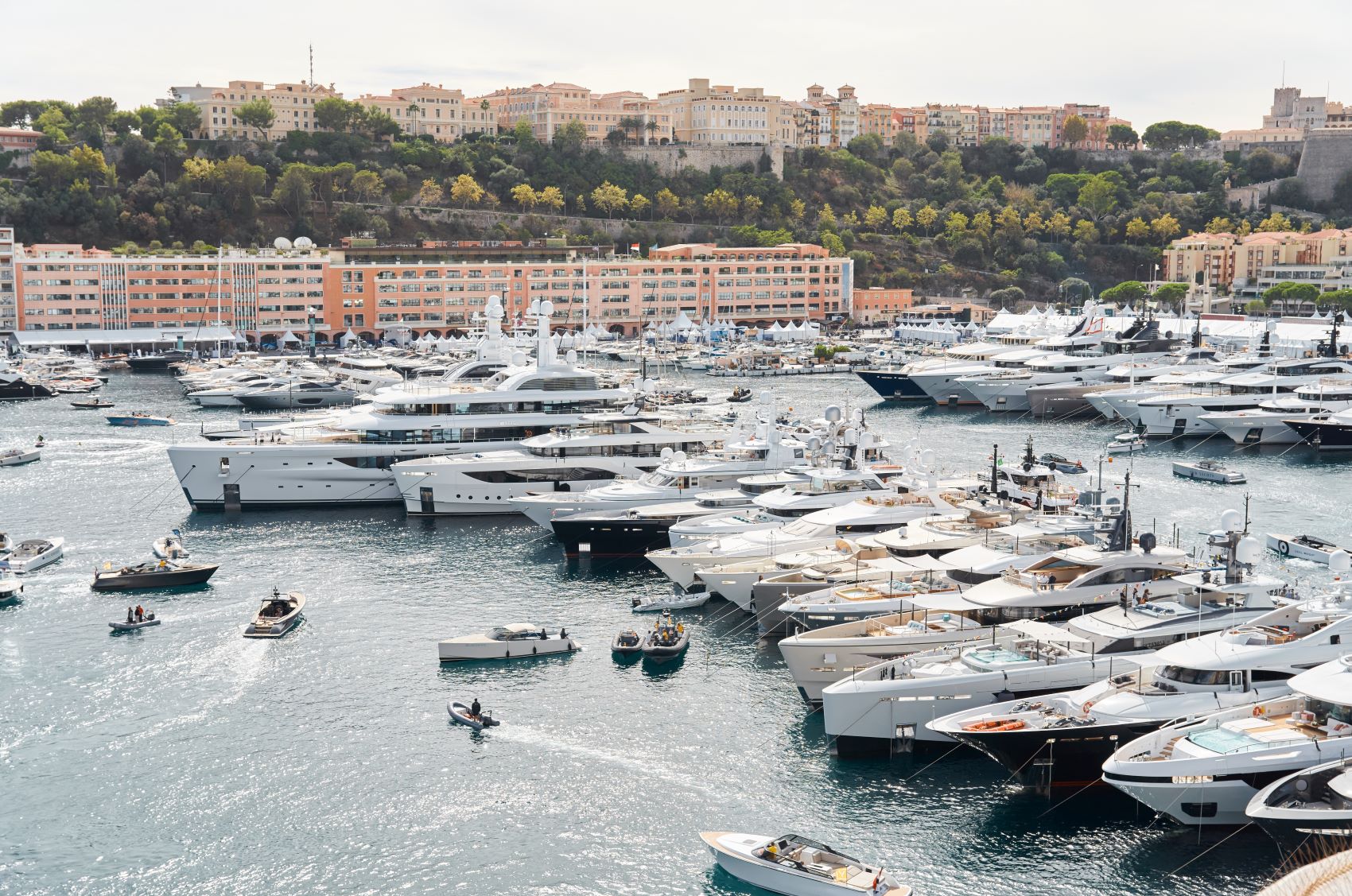 Luxury yachts are docked in a busy marina, surrounded by hills and buildings, exemplifying modern marine elegance.