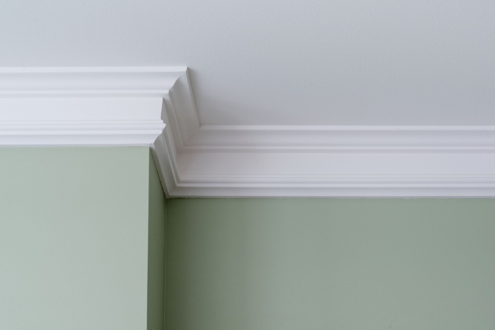 Plaster coving at the junction of a white ceiling and light green wall, showcasing style options for home improvement.