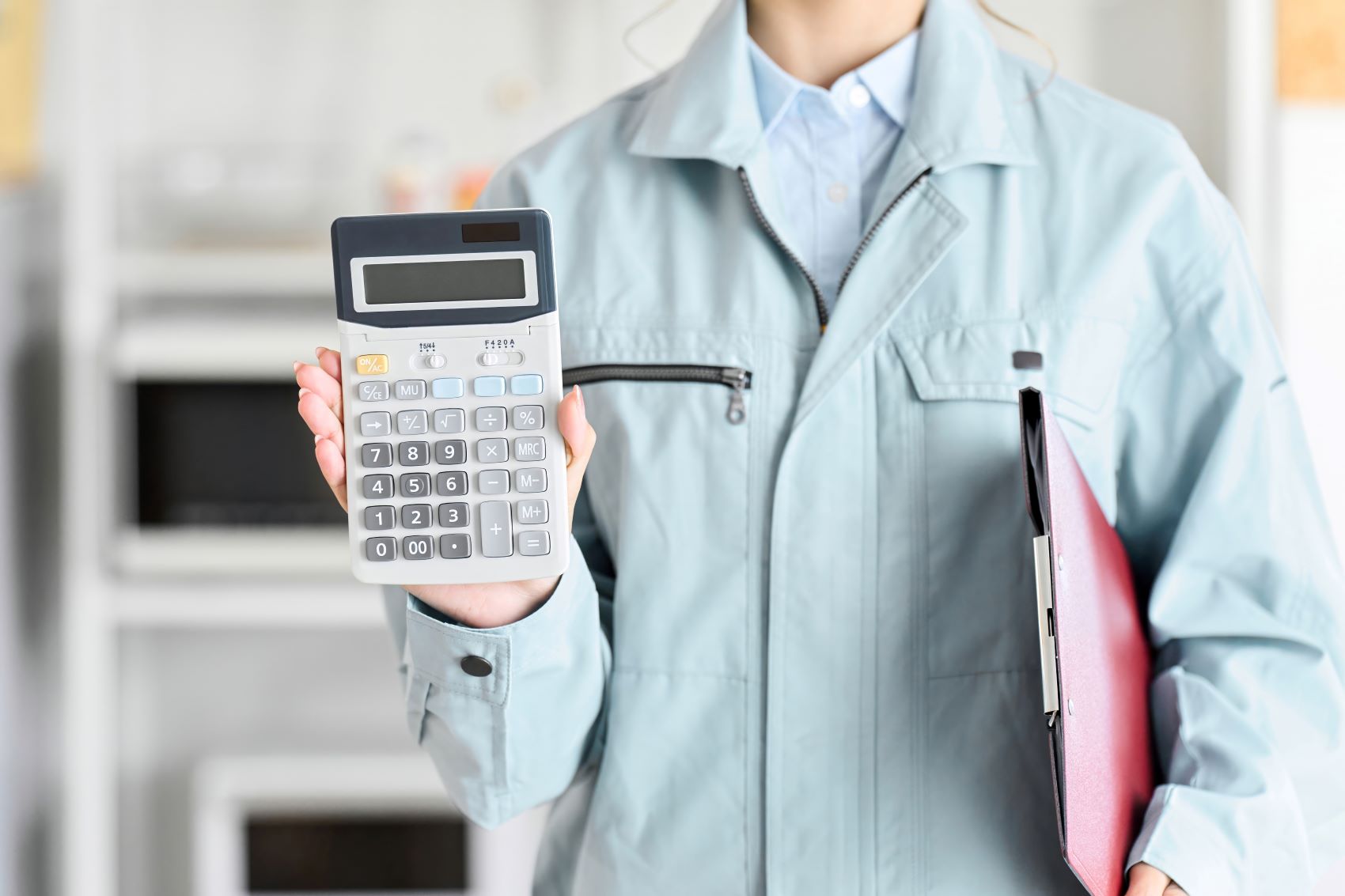 A person in a light jacket holds a calculator and a folder, emphasizing budgeting for moving expenses.