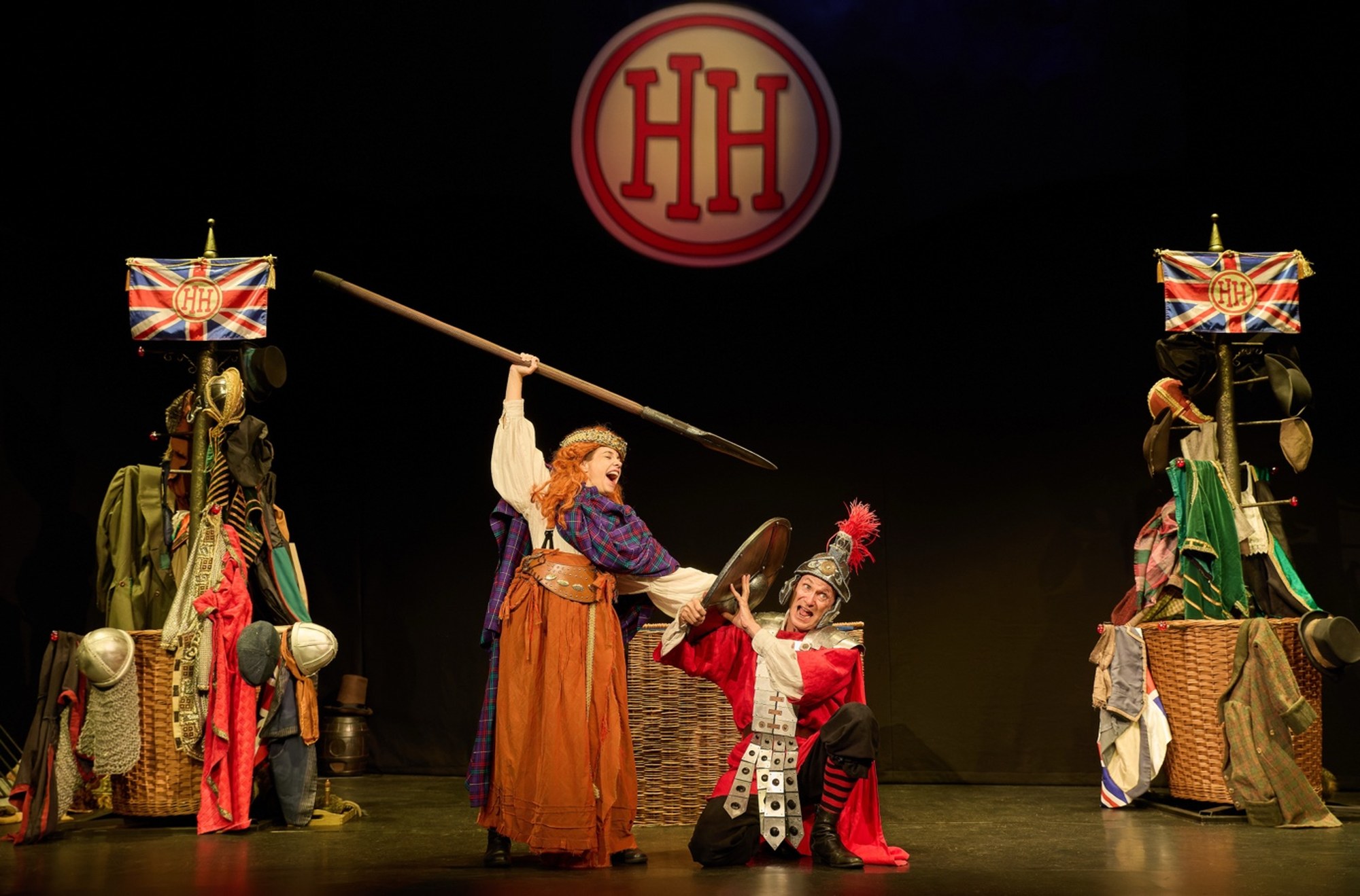 A comedic performance featuring actors in historical costumes, with one wielding a spear and the other in a Roman outfit.