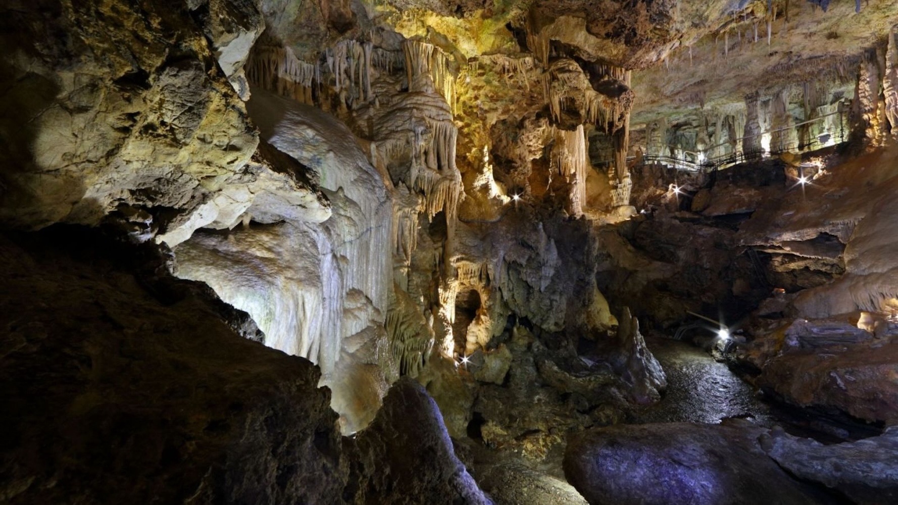 Stalactites and stalagmites illuminated inside a cave, showcasing natural formations and rock textures.
