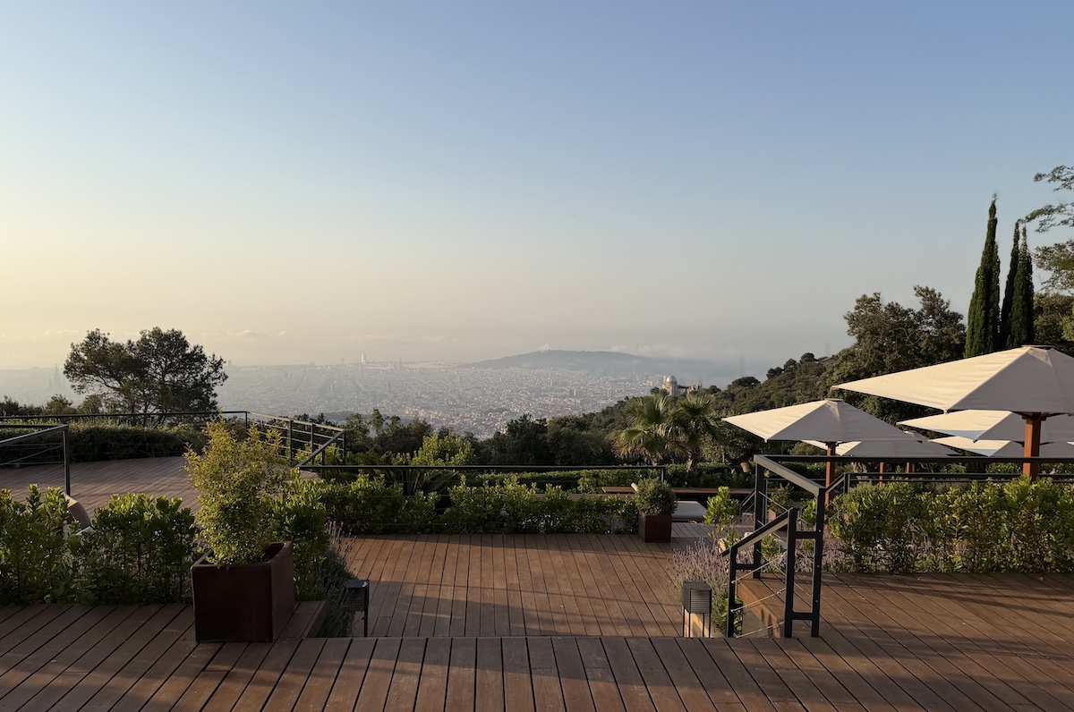 Panoramic view of Barcelona from a terrace at METT Barcelona, featuring greenery, wooden decking, and umbrellas.