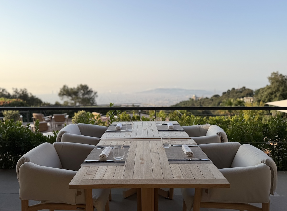 A rooftop dining area with a wooden table set for a meal, overlooking a stunning city landscape.