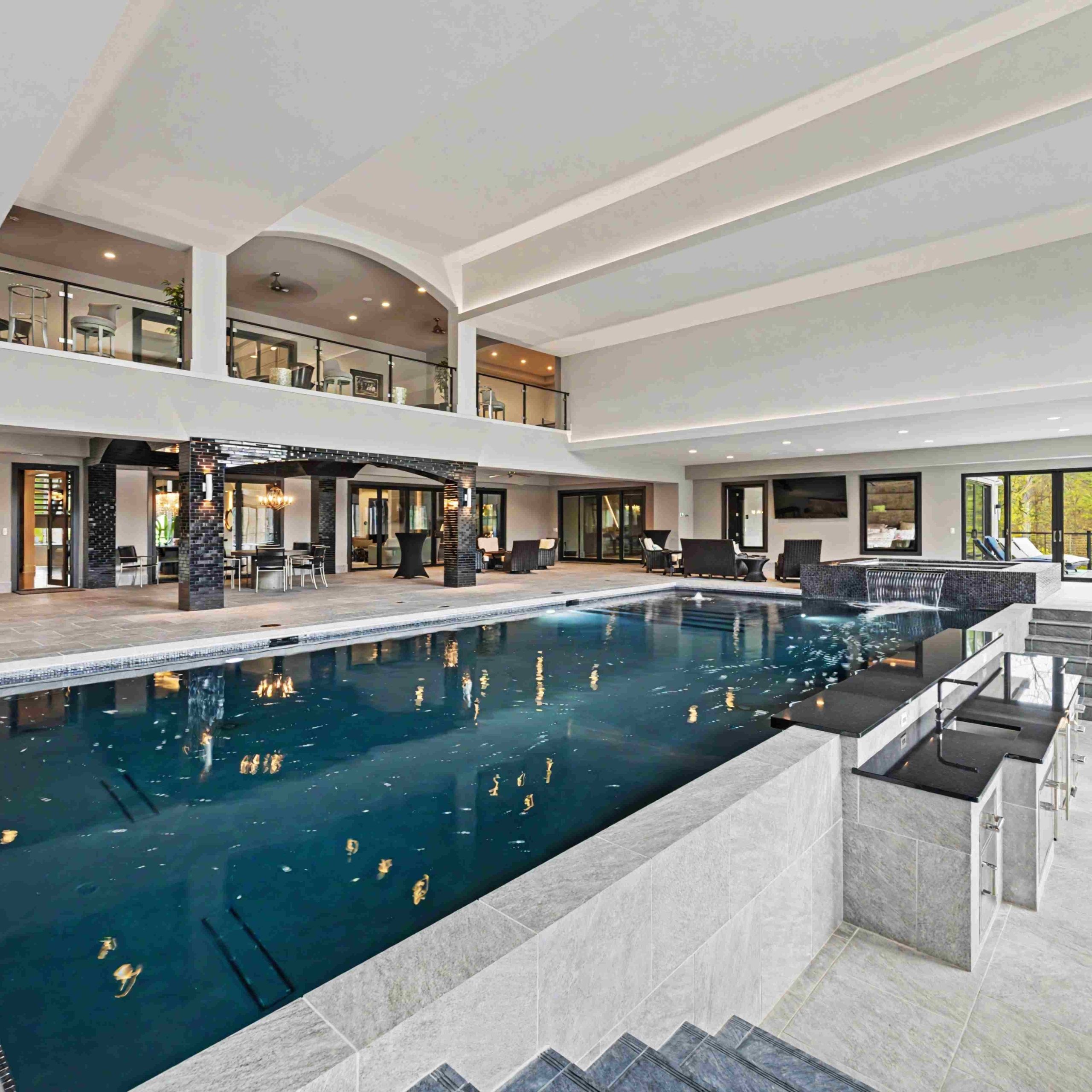Indoor luxury pool with modern architecture, spacious lounging area, and large windows overlooking a serene landscape.