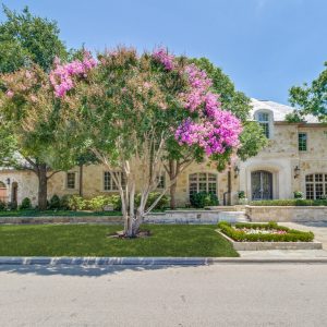 Luxurious stone home surrounded by lush trees and vibrant flowering plants in University Park.