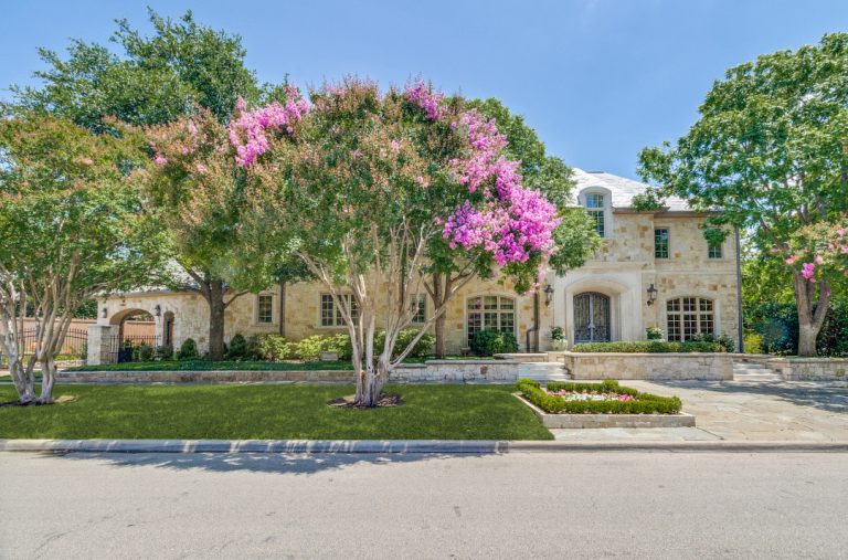 Luxurious stone home surrounded by lush trees and vibrant flowering plants in University Park.