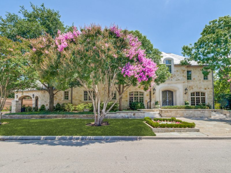 Luxurious stone home surrounded by lush trees and vibrant flowering plants in University Park.