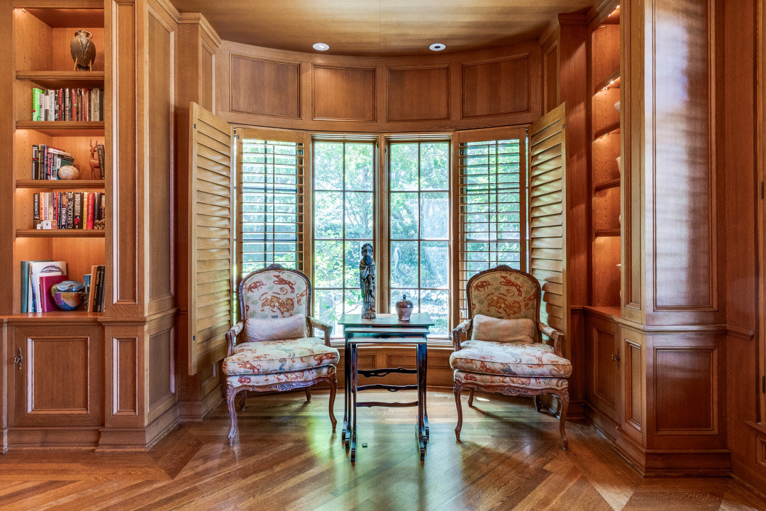 Cozy reading nook featuring two elegant chairs, a small table, and built-in shelves with books, surrounded by large windows.