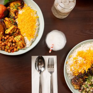 Vibrant Persian dishes featuring fluffy rice, grilled meats, roasted vegetables, and refreshing beverages on a wooden table.