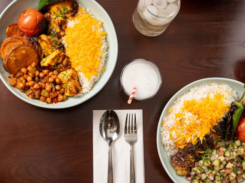 Vibrant Persian dishes featuring fluffy rice, grilled meats, roasted vegetables, and refreshing beverages on a wooden table.