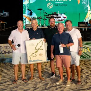 Five men stand together on the sand, holding a framed map, celebrating at the Stars & Stripes Tournament event.