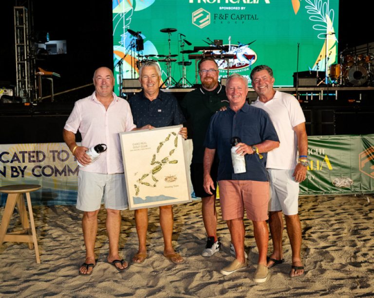 Five men stand together on the sand, holding a framed map, celebrating at the Stars & Stripes Tournament event.